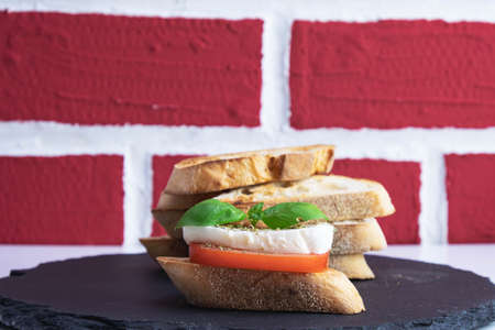 white bread croutons with mozzarella, basil and tomato on a stone stand on a brick background
