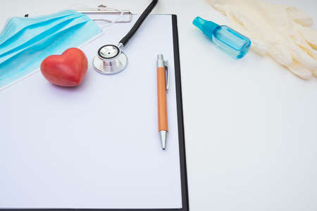gloves, face mask, stethoscope and red stone artificial heart, note sheet and pen on a white...
