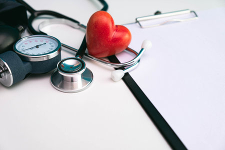 red stone heart, stethoscope, note sheet and pressure meter on white background on tableの写真素材