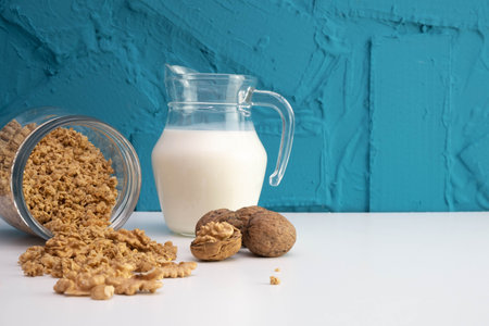 peeled walnuts in a glass jar are scattered on the table, next to there is a jug of milk, on a white backgroundの写真素材