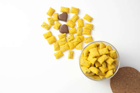 crispy cornflakes in a glass jar stand on the table, next to it are pralines of chocolate, on a...