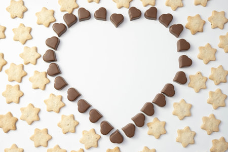 pralines of chocolate are laid out in the shape of a heart, outside lie the cookies in the shape of a star, on a white backgroundの写真素材