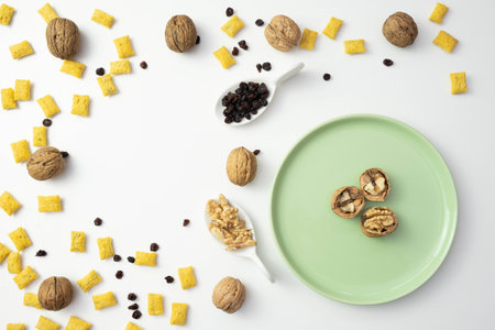 Cornflakes and raisins are scattered on the table, near walnuts on a white backgroundの写真素材