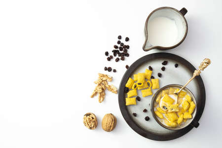 walnuts and raisins lie on the table next to milk and cornflakes in a cup, on a white background