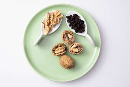 Walnuts and raisins lie on a green plate, on a white background