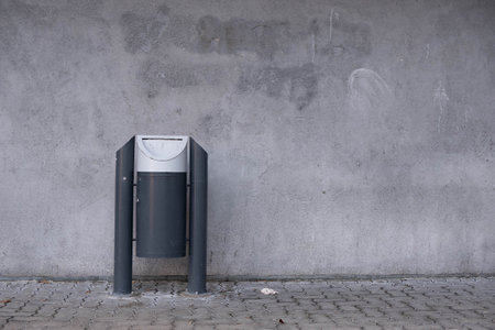 A lone trash can stands near the wall, on the streetの写真素材