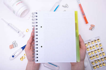 the notebook lies on the hands, and behind the thermometer, syringe, pills and various medical...