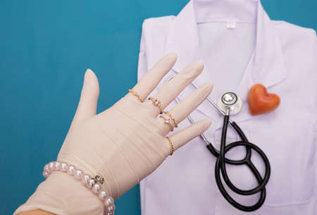 on the table lie the doctor's clothes and a stethoscope, on top of the doctor's hand in gloves and wearing jewelry, on a white backgroundの写真素材