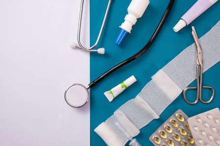 bandages, scissors, ointments, stethoscope, pills and a white piece of paper lie on the table, on a blue backgroundの写真素材