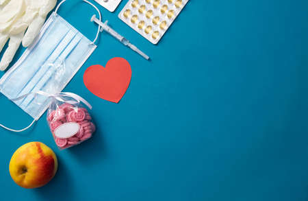 syringe, gloves, heart, apple, pills, mask lie on the table, on a blue backgroundの写真素材
