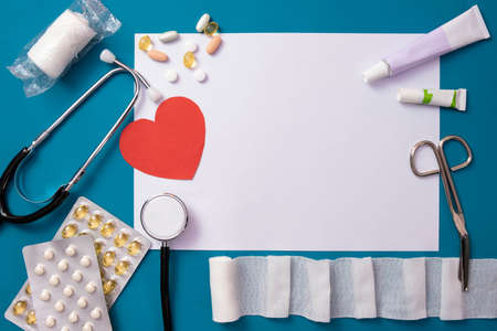 bandages, scissors, red heart, stethoscope, pills and a white piece of paper lie on the table, on a...