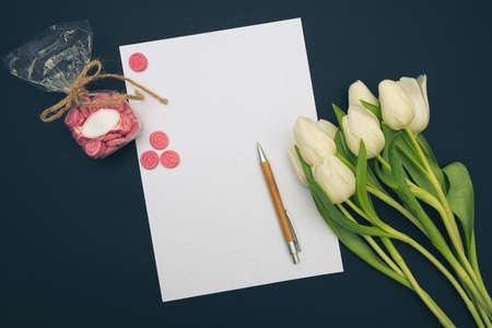 bouquet of white tulips, blank sheet of paper, pen and lollipops on black background
