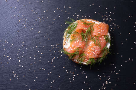 bun with smoked fish, fresh cream, sprinkled with dill and sesame seeds, dill branches on a black background, close-upの写真素材