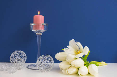 bouquet of white tulips, glass candlestick with a lit candle and decorative metal balls, blue...