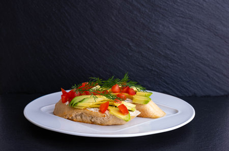 canapes of avocado slices and a slice of tomato with dill on a white plate and black background
