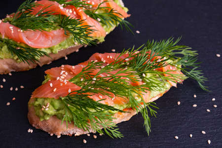 two mouth-watering crispy canapes with avocado and smoked salmon fillet and fresh dill sprigs and...