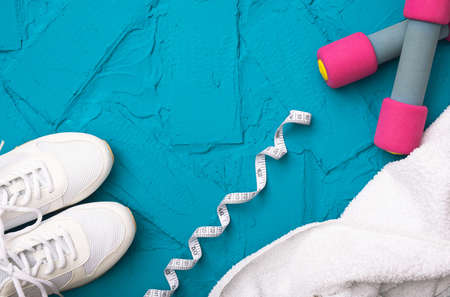 fitness at home - white sneakers, towel, measurement tape and dumbbells, lie on a blue backgroundの写真素材