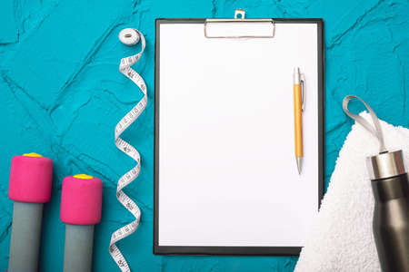 fitness at home - dumbbells, towel, water bottle, measurement tape and sheet of paper on blue backgroundの写真素材