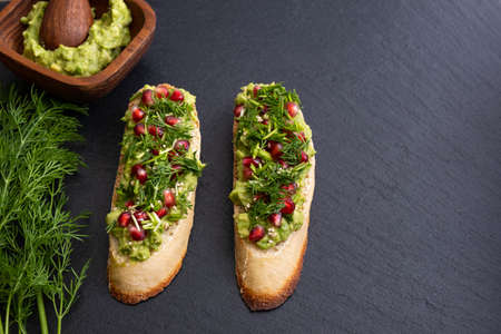 healthy and tasty avocado canapes, sprinkled with ripe pomegranate seeds, sesame seeds and fragrant...