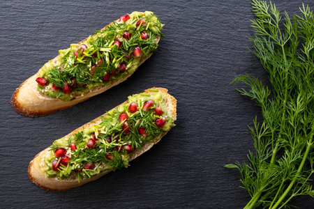two snacks - avocado, sprinkled with ripe pomegranate seeds, sesame seeds and fragrant fresh dill,...