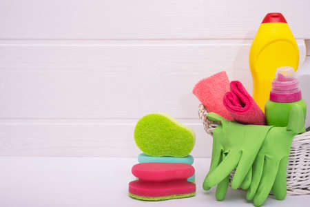 wicker basket with colored household cleaning liquids, colored brushes and rags, gloves on a white backgroundの写真素材