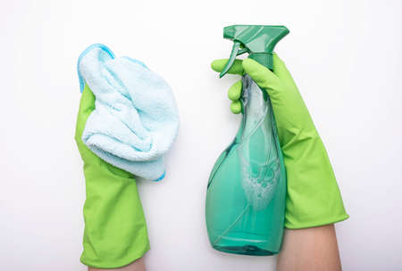 hands in gloves hold detergent and a rag for cleaning the house, against white backgroundの写真素材