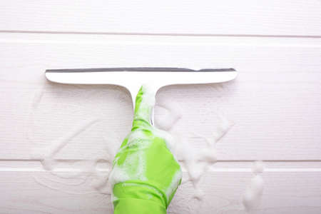 a hand in a green glove holds a brush and wipes a soapy wall in a bathroom