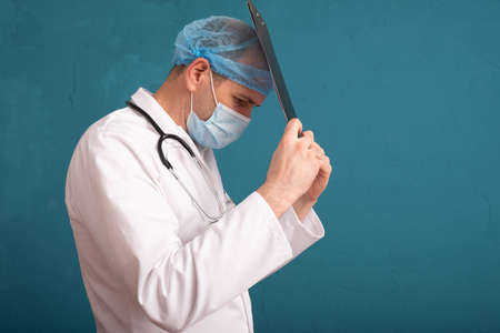 doctor in a white coat and a stethoscope on his shoulders holds a folder near his head, blue...