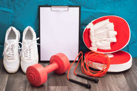 red - dumbbells, jump rope and kick pads, note board and white sneakers, close-up and blue...
