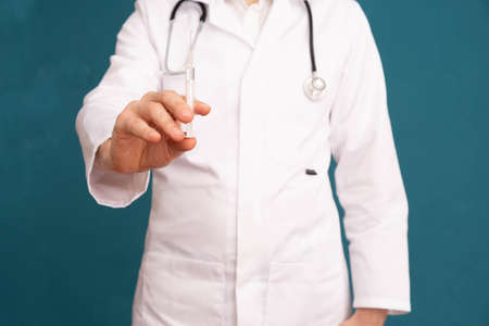 doctor on the shoulders of a stethoscope, holding a syringe with a vaccine, on a blue backgroundの写真素材