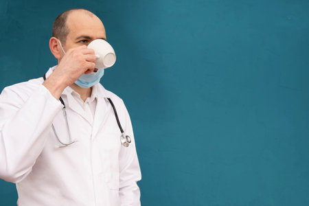 doctor wearing a stethoscope on his shoulders and pauses drinking coffee, blue backgroundの写真素材