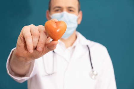 a doctor in a mask holds and shows a heart, blue background