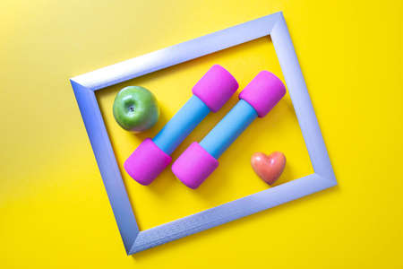 in a metal frame are pink dumbbells, a green apple and a heart, yellow backgroundの写真素材