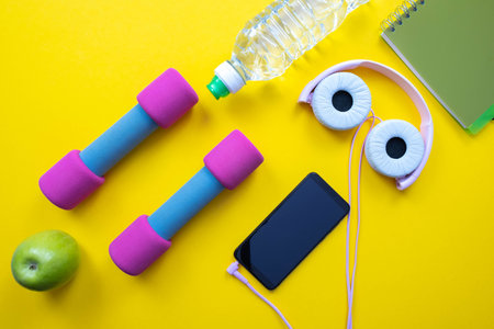 cell phone with headphones, dumbbells and water bottle and apple, on yellow background and close-upの写真素材