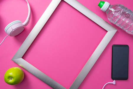 metal frame, cell phone with headphones, bottle of water and green apple on a generic pink backgroundの写真素材