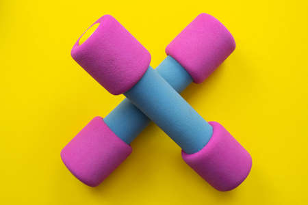 pink dumbbells lie on a yellow background, close-up