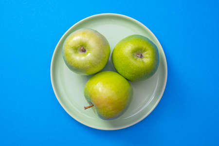a green plate with green apples stands in the center of a blue background, close-upの写真素材