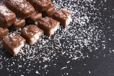 chocolate bars with coconut filling sprinkled with coconut flakes on a black backgroundの写真素材