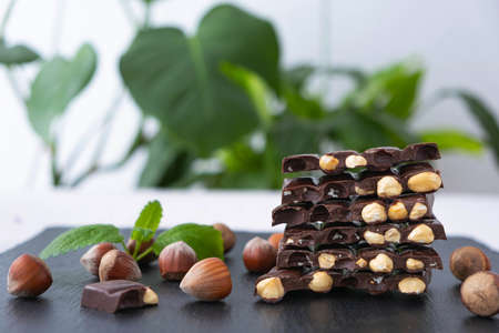 broken bars of dark chocolate with nuts, scattered unpeeled hazelnuts, mint petals on a black backgroundの写真素材