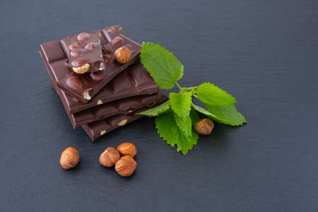 chocolate bars with hazelnuts, next to mint and hazelnuts, on a black background