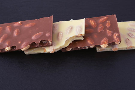 bars of white and milk chocolate with almonds inside, lie in a row on a black background