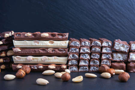 lined in a row different chocolate bars with nuts and coconut, scattered nuts on a black backgroundの写真素材