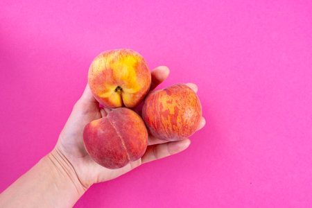 three ripe peaches in hand, on a pink background, close-upの写真素材