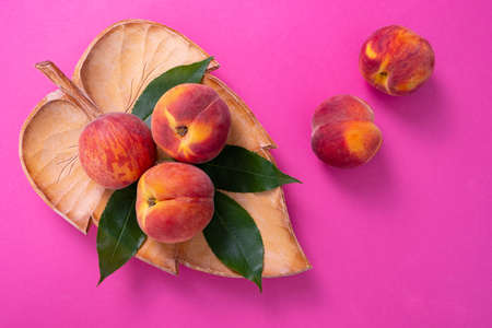 three ripe peaches are in a carved wooden plate, green foliage and two peaches side by side, close-upの写真素材