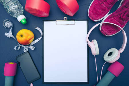 sports equipment - clothes, sneakers, dumbbells apple and a bottle of water, mobile phone with headphones, measuring tape, blue backgroundの写真素材