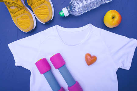 white t-shirt and yellow sneakers, water bottle and apple, dumbbells, blue backgroundの写真素材
