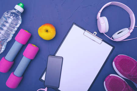 sports equipment - sneakers, dumbbells apple and bottle of water, mobile phone with headphones, blue backgroundの写真素材