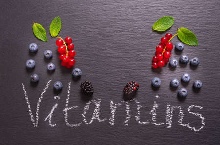 sprinkled ripe blueberry, currant and blackberry and mint leaves and an inscription on a black backgroundの写真素材