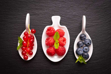 ripe berry - raspberries, red currants and blueberries and mint leaves, lie in a white dish on a black backgroundの写真素材