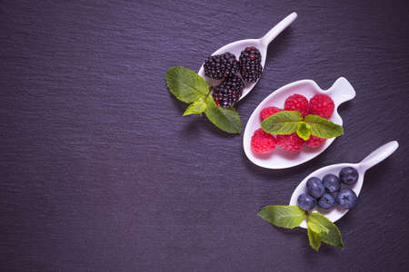 ripe berry in a white dish - blackberries, raspberries and blueberries, on a black backgroundの写真素材
